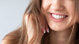 Young lady with brunette hair smiling with exposed teeth against a light coloured background
