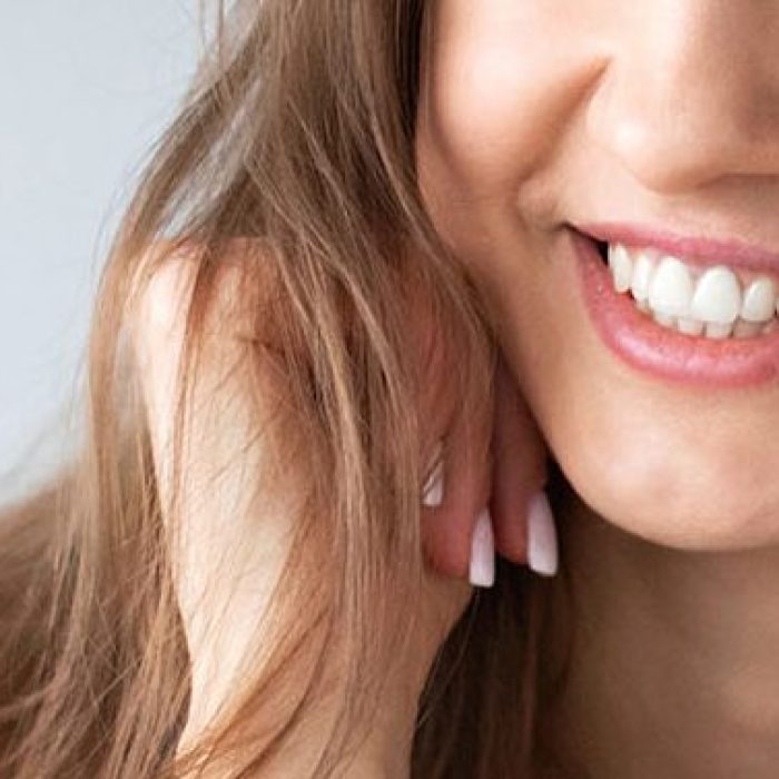 Young lady with brunette hair smiling with exposed teeth against a light coloured background